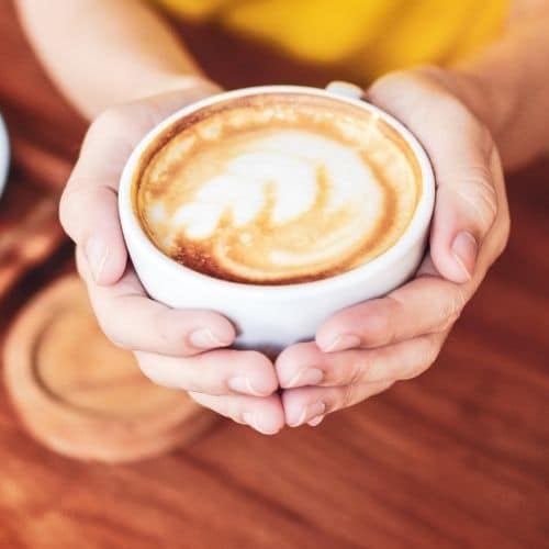 hands holding frothy cup of coffee