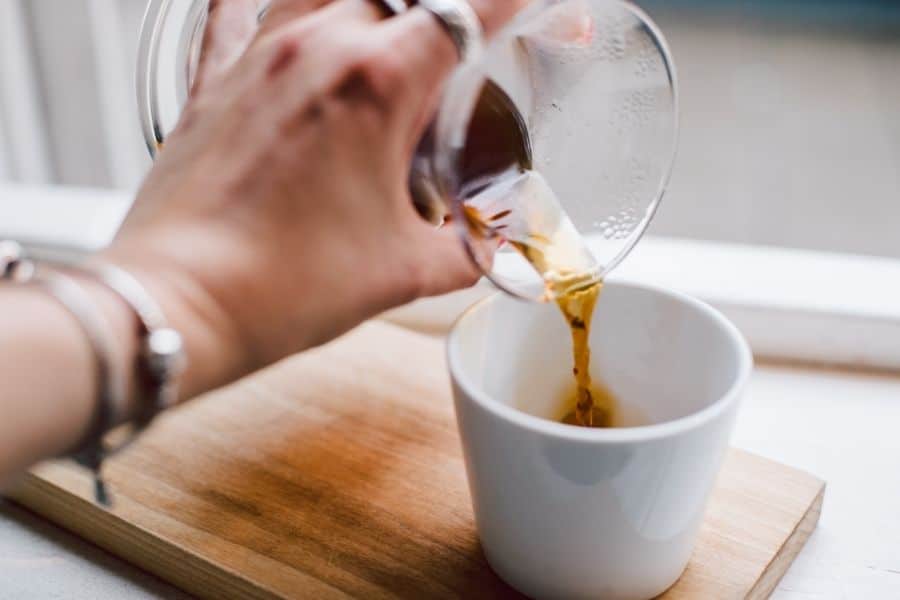 ladies hand pouring cold brew coffee from a carafe into a mug