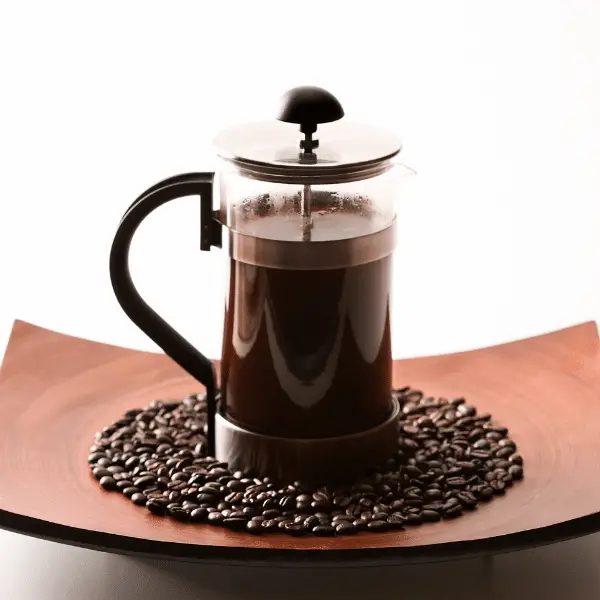 french press on plate of coffee beans